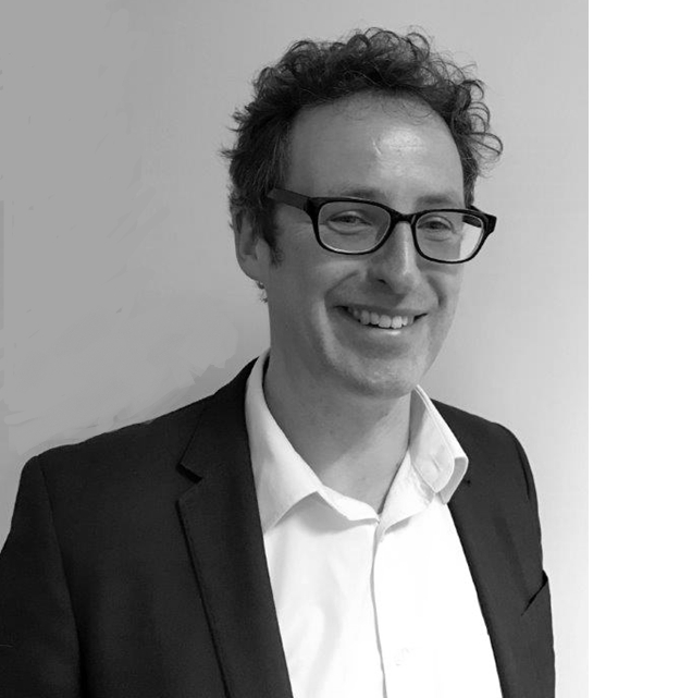 Black and white portrait photograph of a white male with short curly hair and dark rimmed glasses